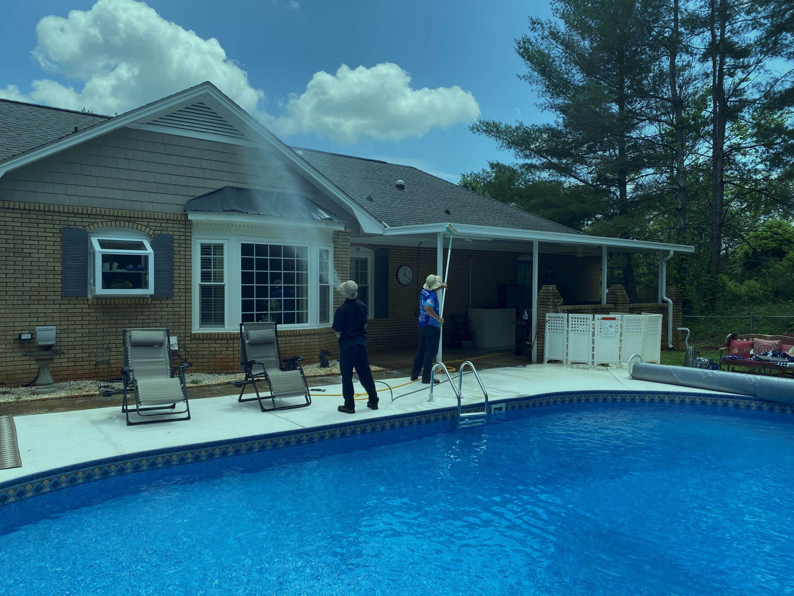 HydroClean team pressure washing home exterior near pool
